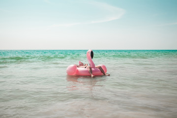A man is having fun on pink flamingo inflatable pool float in the turquoise sea with white waves