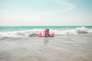Fototapeta na wymiar A man is having fun on pink flamingo inflatable pool float in the turquoise sea with white waves