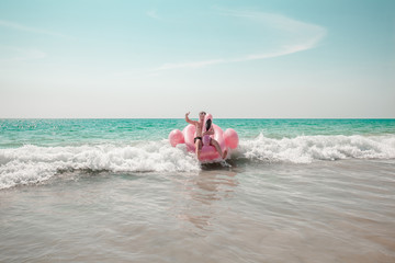 A man is having fun on pink flamingo inflatable pool float in the turquoise sea with white waves