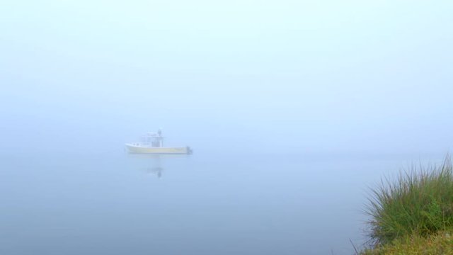 Commercial lobster boat moored in a small tranquil New England cove at dawn.  Foggy lighting with no horizon line visible.
