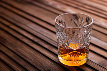 Rustic still life with whiskey and snacks. Crystal glass with a beautiful pattern on a wooden table. Snack for whiskey on crumpled paper olives, crackers, cheese, almonds, pear, apple.