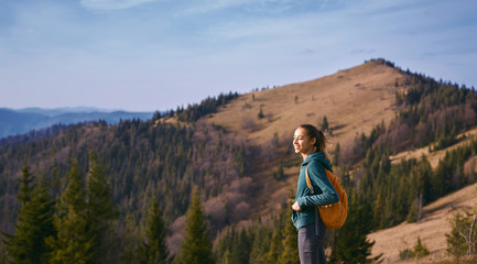Fototapeta premium image of a happy woman hiker standing on the slope of mountain ridge on the mountains and blue sky background. the woman is happy and looks around with delight