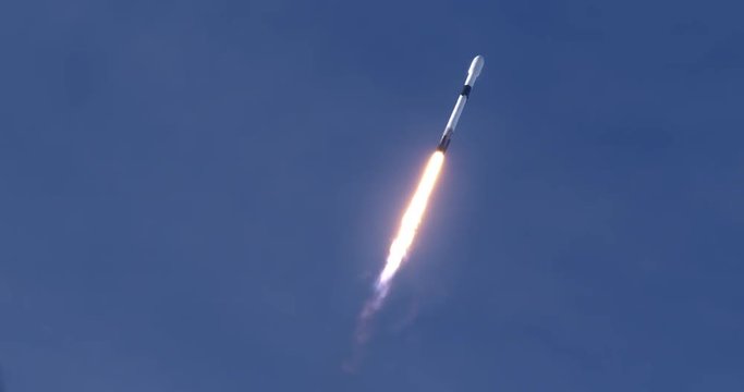 Rocket launching into space through blue skies and clouds. Flames and smoke trail behind the rocket. 4K video at 120 fps slow motion. With audio.
