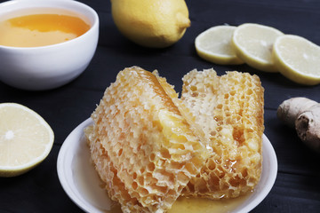 Traditional medicine. Honey and bee honeycombs on a black wooden background. Healing tea. Ingredients for tea. Honey for tea. Ginger and lemon. Copy space. Design elements