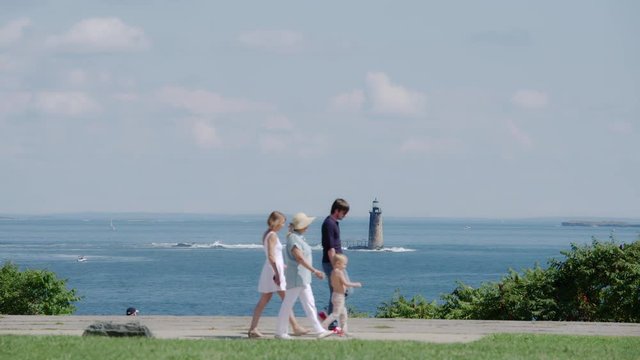 Family walks in front of Ram Island Ledge Light Station in Casco Bay near Portland, Maine on a nice summer day with blue water