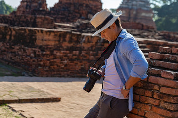 Eastern Asia summer holidays. Caucasian man tourist from back looking at Wat Chaiwatthanaram temple. Travelers take pictures with DSLR cameras. Travel in old city of Ayutthaya, Thailand. Asia tourist.