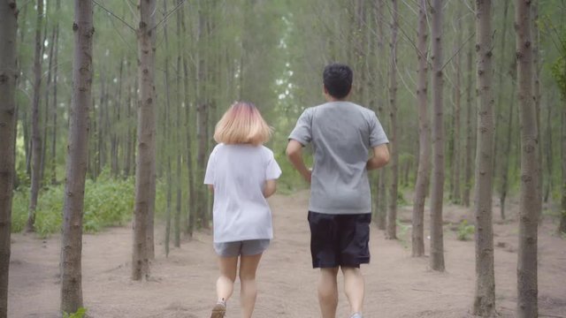 Healthy young athletic sporty Asian runner man and woman in sports clothing running and jogging on forest trail. Lifestyle fit and active women exercise in the forest concept.