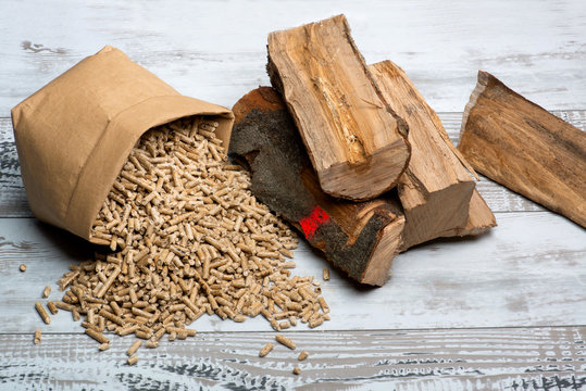 Scheitholz und Holzpellets liegen nebeneinander auf Holztisch,direkter Vergleich von Brennstoffen