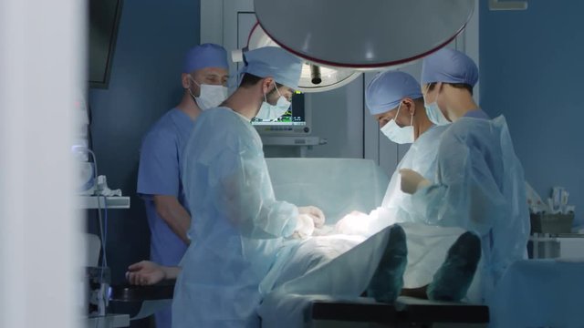 Group of four concentrated medical professionals performing surgery on patient in operating room at hospital
