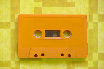 An old cassette tape of a yellow color with orange background