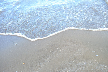 A curve of white sea waves on a beautiful sand beach in bright day 
