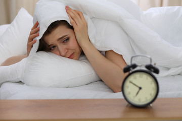 Beautiful young woman don't want to wake up for work early morning. Unpleasant ringing alarm clock