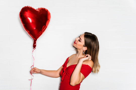 Beautiful young woman in red dress holding heart shaped balloon - valentines day