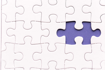 Unfinished white jigsaw puzzle pieces. One missing jigsaw piece on purple background