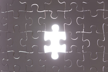 Unfinished white jigsaw puzzle pieces. One missing jigsaw piece on white back light background