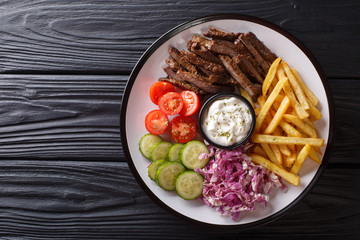 Freshly cooked shawarma plate with beef, french fries, vegetables and sauce close-up. horizontal top view