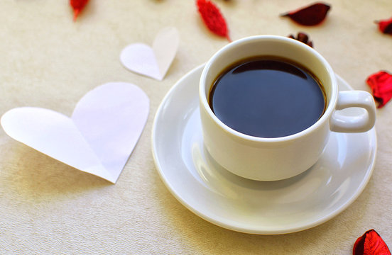 Hot mug with black coffee, heart shaped postcard and rose petals. Romance and love.