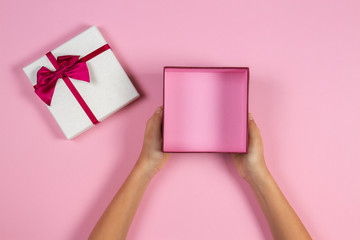Hands holding open empty present gift box on pastel pink background, top view