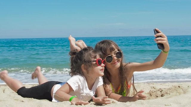 Children taking pictures on beach. Happy little girls are photographed lying on the sand at the beach.