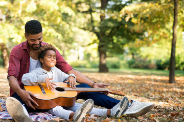 Little girl in fathers embrace learning to play guitar. Cuteness all around.