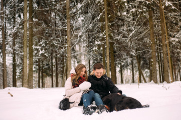 Obraz premium young couple having fun in winter park with their dog. Hugging young couple in love walking with dog outdoors in snowy winter