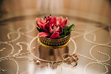 wedding rings are on the glass table next to the red orchids in the box