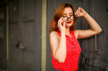 Fototapeta premium Attractive redhaired woman in eyeglasses, wear on red blouse and jeans skirt posing.