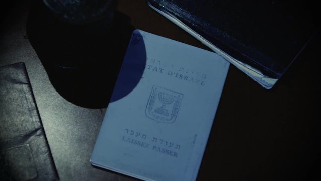 Gloved thief with flashlight steals an Israeli passport from a pile of documents