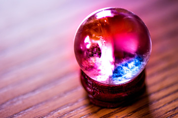 Fortune telling. A macro shot of purple, blue and turquoise glass balls on a wooden pad, with sun reflections, bubbles and a rainbow in it,standing on a pine dining table in the middle of a kitchen.