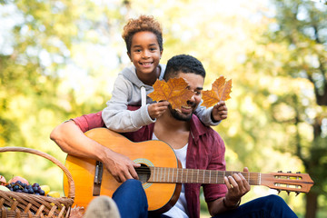 Happy moment of family time. Father playing guitar while daughter holding tree leaves. Happiness.