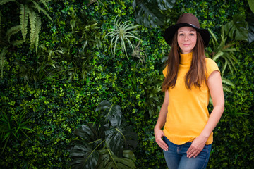 Young woman with hat posing by green wall