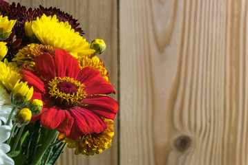 A fragment of a bouquet with beautiful red and yellow flowers on the left on a wooden background. Right place for text.