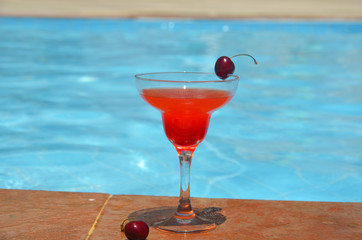 Tasty red cocktail background swimming pool. Margarita cocktail with a glass of cherries.