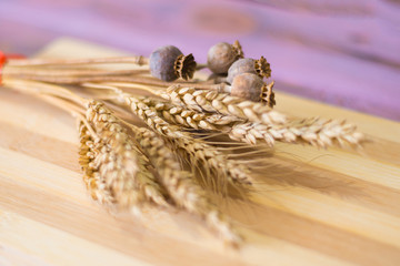 Ripe wheat spikelets and poppy stems on a wooden background.