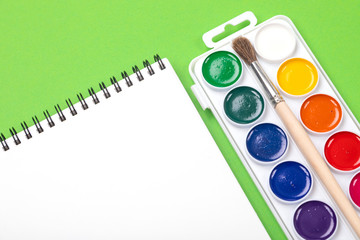 Watercolor paints and brushes with album for drawing isolated on green background top view