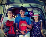three children sitting on a car before going on holiday