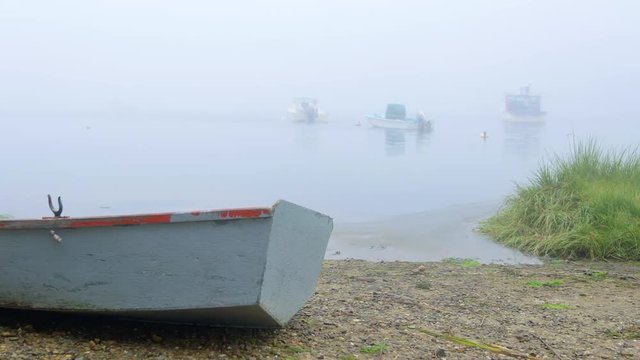 Peaceful shot of rustic wooden rowboat dinghy beached on rocky shore on Cape Cod. Camera pans left.