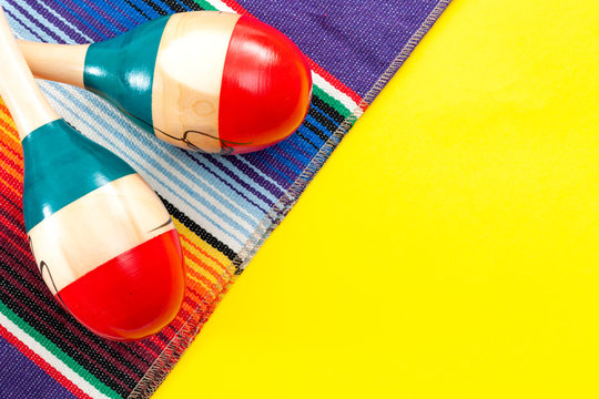 Mexican fiesta and Cinco de Mayo party concept theme with minimalist image of red and blue maracas and traditional colorful rug called a serape on yellow background with copy space for text
