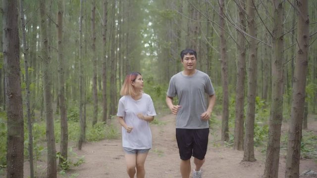 Healthy young athletic sporty Asian runner man and woman in sports clothing running and jogging on forest trail. Lifestyle fit and active women exercise in the forest concept.