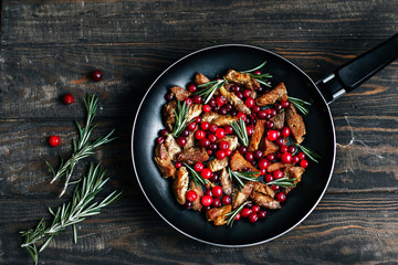 Roast pork with cranberries, olives and rosemary in a pan on a dark wooden table top view