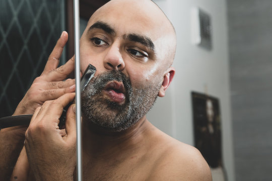 40 year old British Asian male grooming - looking in the mirror - using a cut throat razor. 