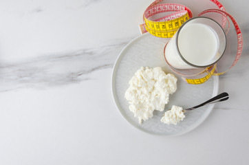 Top view of meal ingredients for milky diet,loss weight.Spoon with cottage cheese and plate,glass with milky product,measuring tape