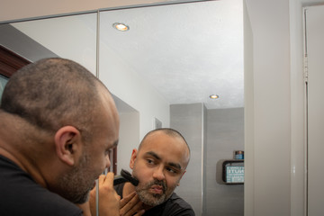 British Asian man, trimming his stubble or beard in front of the mirror.