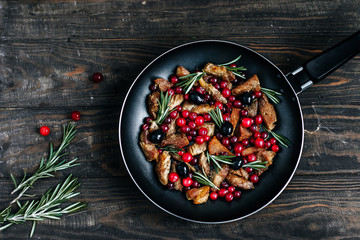 Roast pork with cranberries, olives and rosemary in a pan on a dark wooden table top view