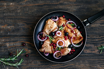 Roast pork with cranberries, olives, rosemary and red onion in a pan on a dark wooden table top view