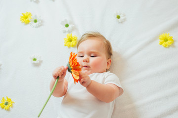 Obraz na płótnie Canvas Beautiful baby holding a flower on white blanket