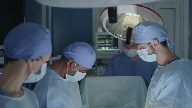Tilt down shot of group of four medical professionals performing surgery in operating theater, assistants helping surgeons