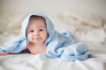 Fototapeten Cute little baby boy, relaxing in bed after bath, smiling happily © Tomsickova