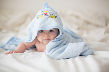 Cute little baby boy, relaxing in bed after bath, smiling happily