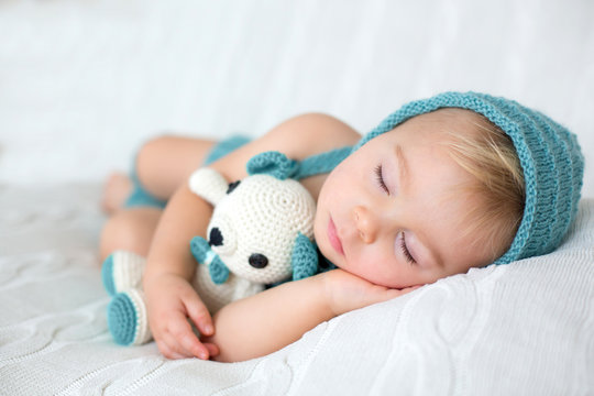 Sweet toddler boy, sleeping with teddy bear toy, cute knitted outfit